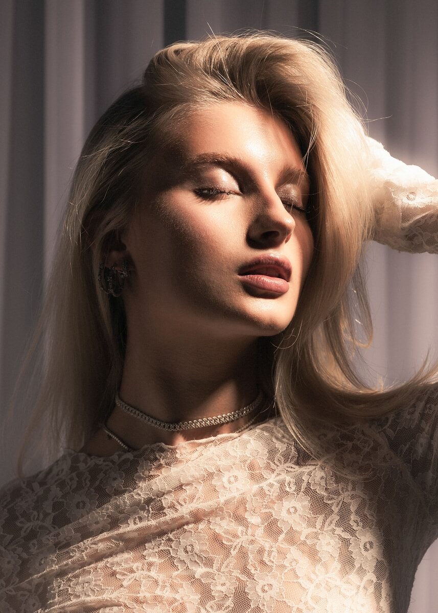 Blonde woman with closed eyes in warm sunlight wearing lace.